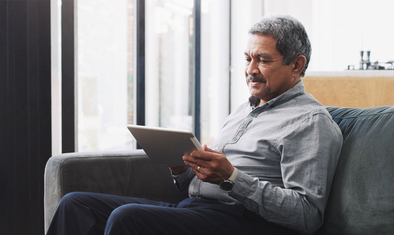An elderly man using a tablet whilst sat in a modern living room