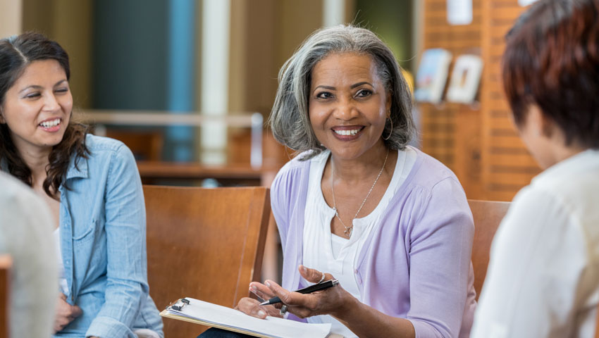 A woman in a purple cardigan smiles as she engages in a group discussion