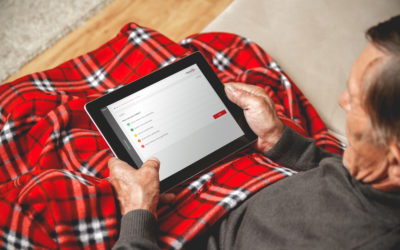 A senior man wrapped up in a red tartan blanket using CliniTouch Vie on a tablet device