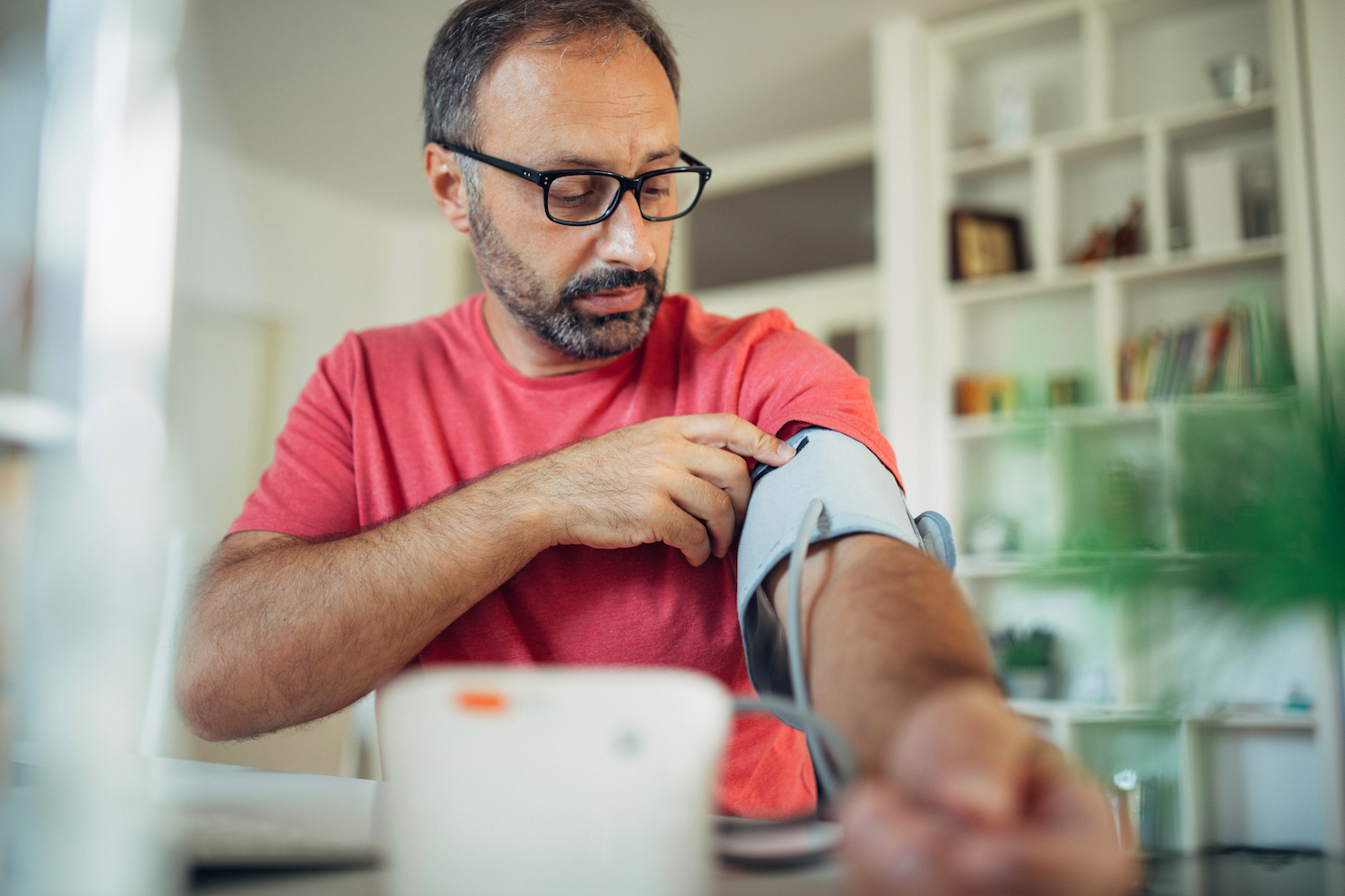 Man with glasses and red t-shirt using a blood pressure cuff at home