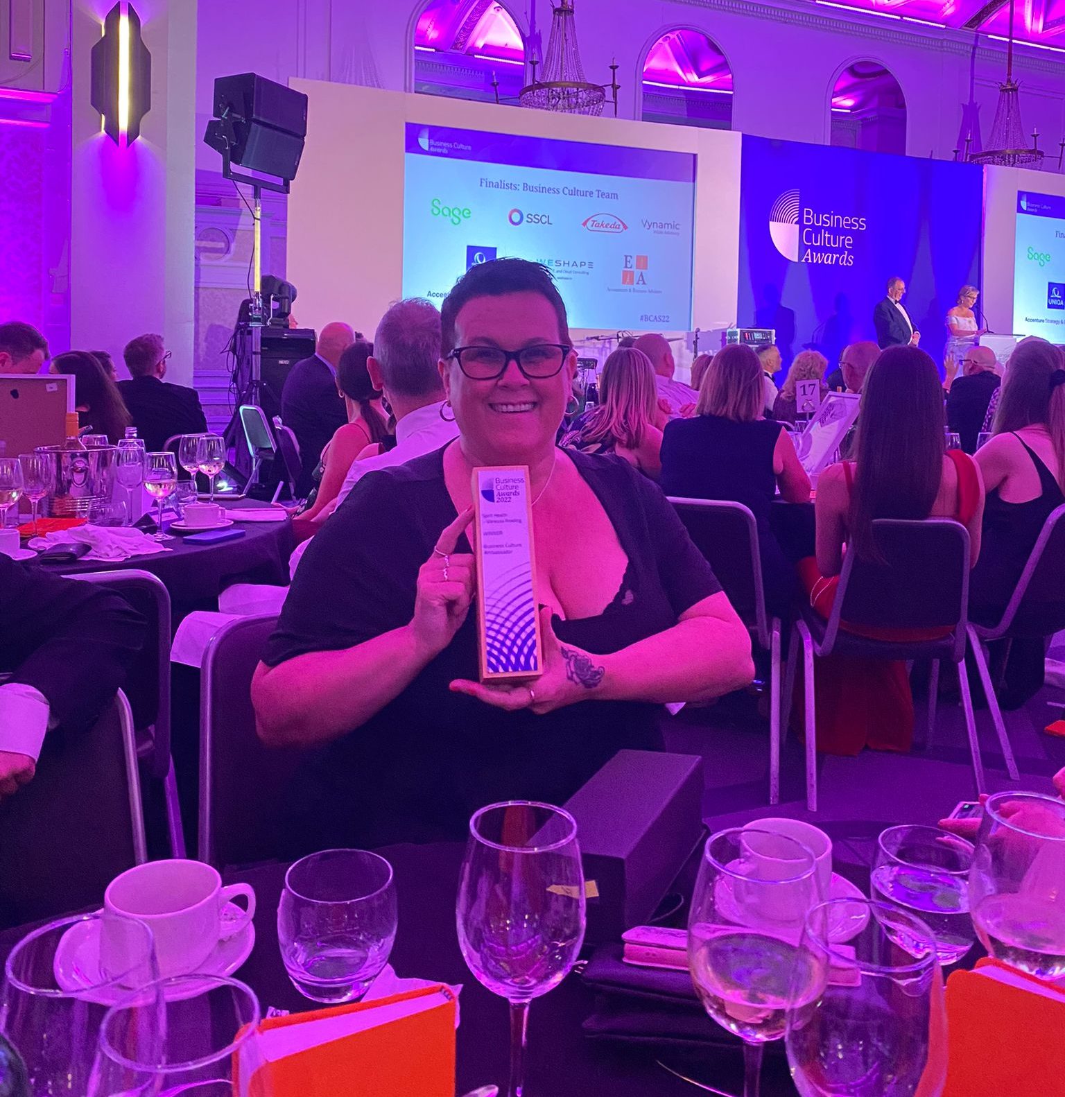 Woman sitting down at an awards dinner, holding an award and smiling