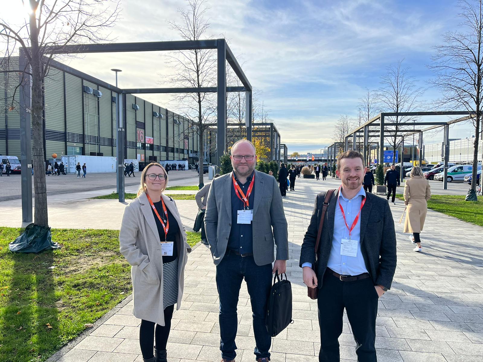 One woman and two men stood in walkway outside MEDICA conference. All smiling