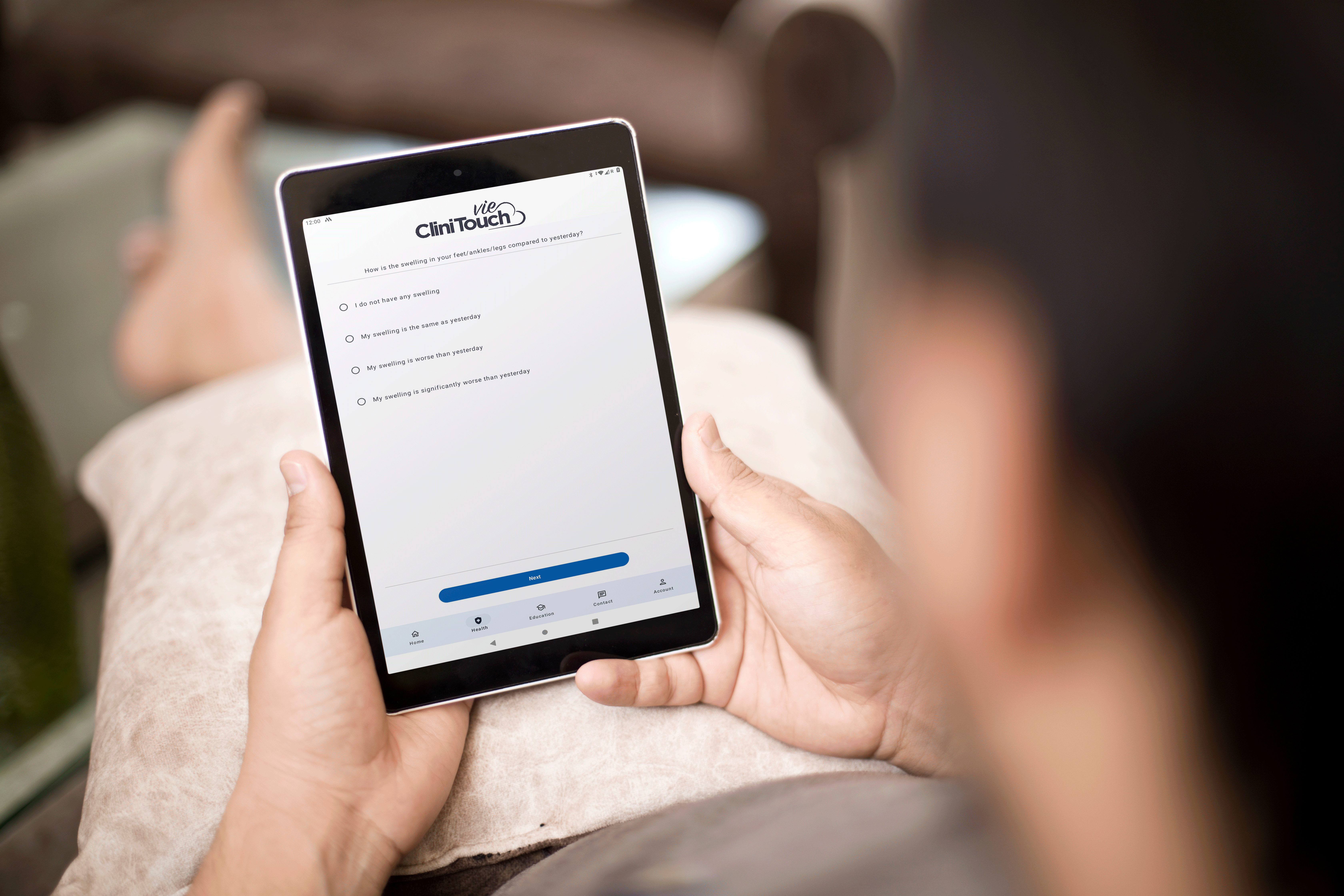 Person sitting down holding a android tablet. They are looking at the remote monitoring app, CliniTouch