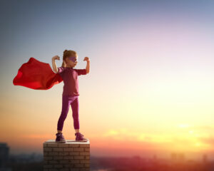 Little child girl plays superhero. Child on the background of sunset sky